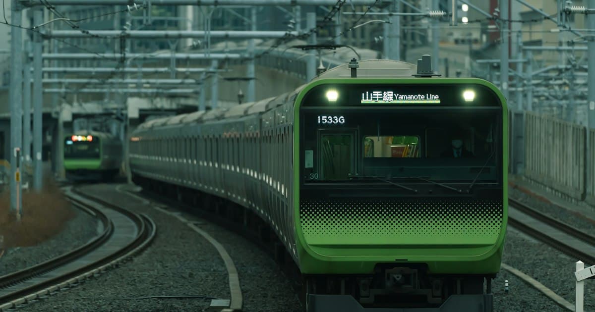 高架の線路を走る緑のラインの電車と、沿線の高いビル